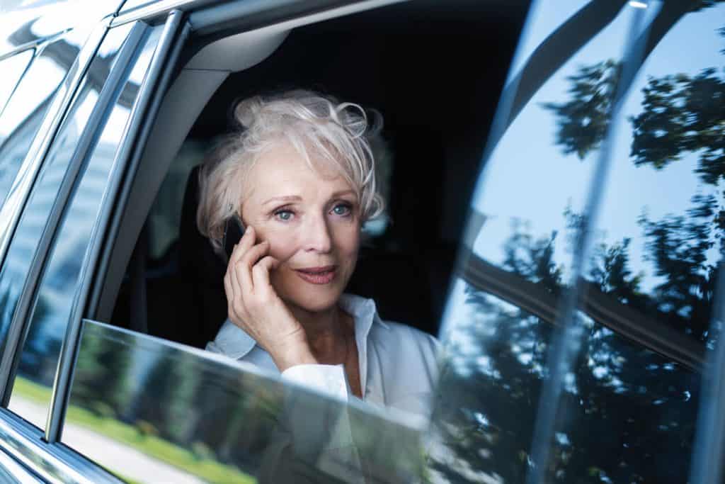 Senior woman in the back of a luxurious car driven by a chauffeur, luxurious assisted living