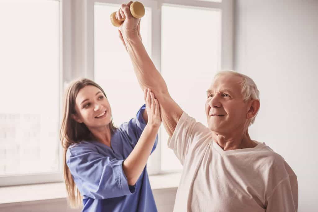 A nurse helping a senior man exercise, assisted living with memory care independent living