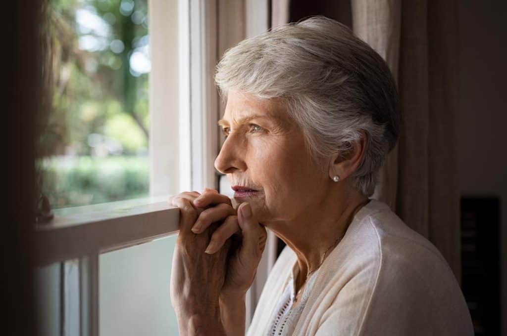A depressed senior looking outside the window, assisted living with memory care mental health mental illness treatment
