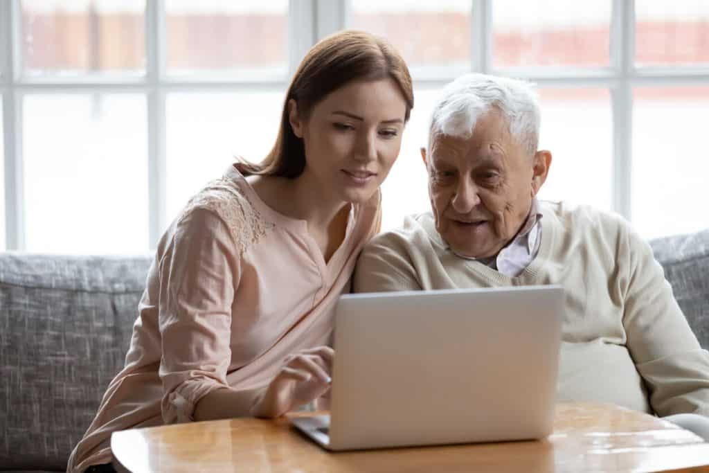 Female caregiver helping elderly man with his computer in a facility, home assisted living