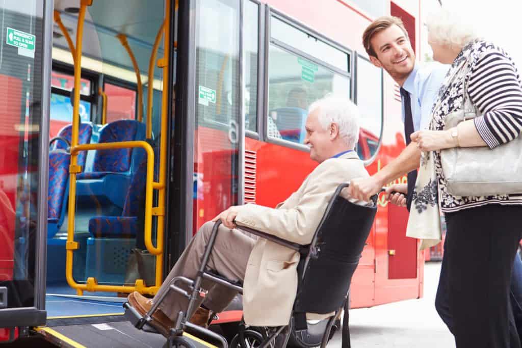 Driver helping elderly man in wheelchair into transportation for seniors 2022, home care for elderly in their own homes