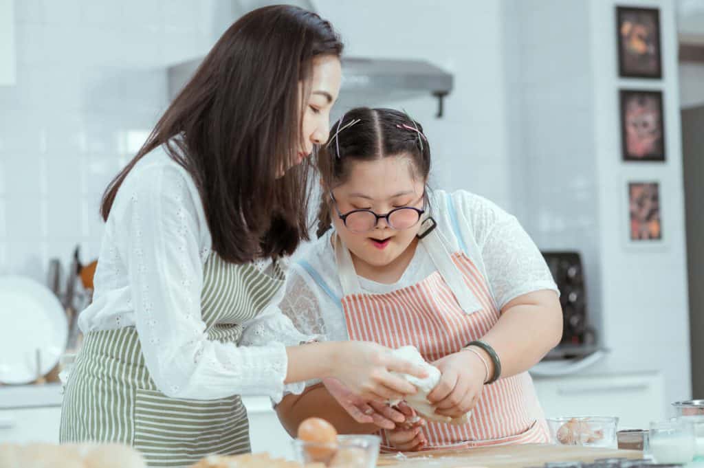 Caregiver and patient with Down’s Syndrome cooking a meal together older persons, inhome care services for disabled