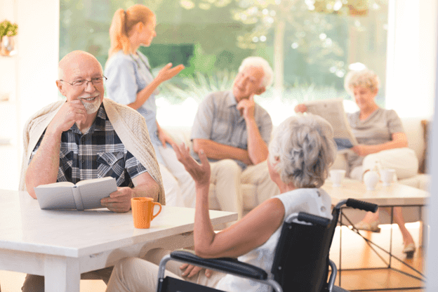 Elderly man chatting with an elderly woman in a wheelchair in a community room social access, home health aides