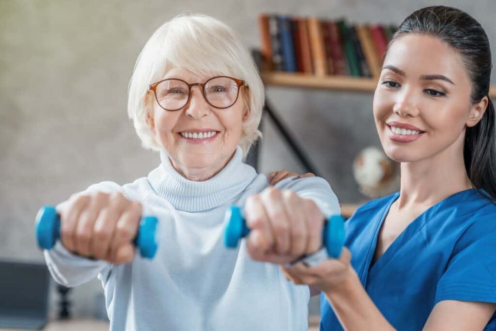 Therapist working with the older woman using dumbells - elder care at home jobs