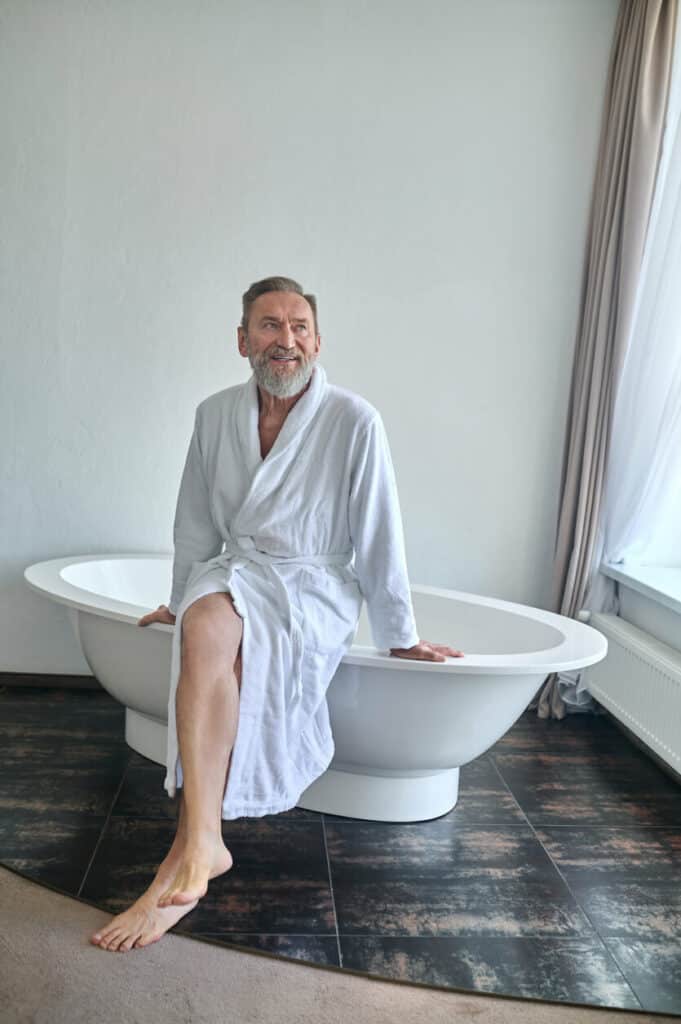 An older adult man waiting for sower assistance in his bathroom