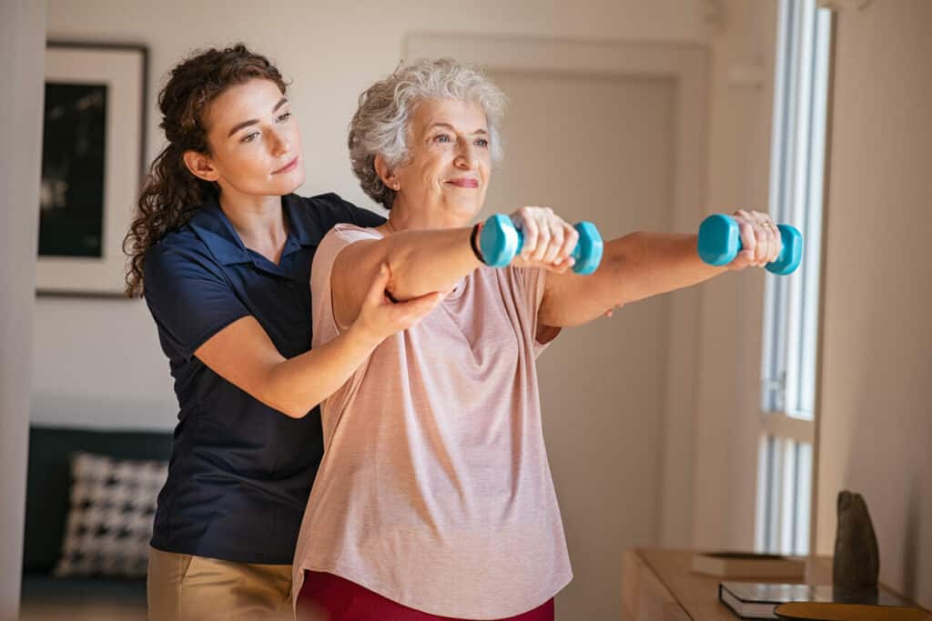 Senior woman lifting small weights with caregiver assistance 2023