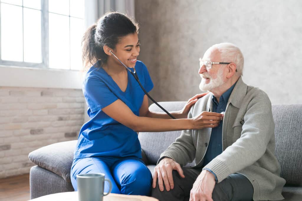 patient young female nurse listening to senior man’s heart and lungs as part of nursing care services safety