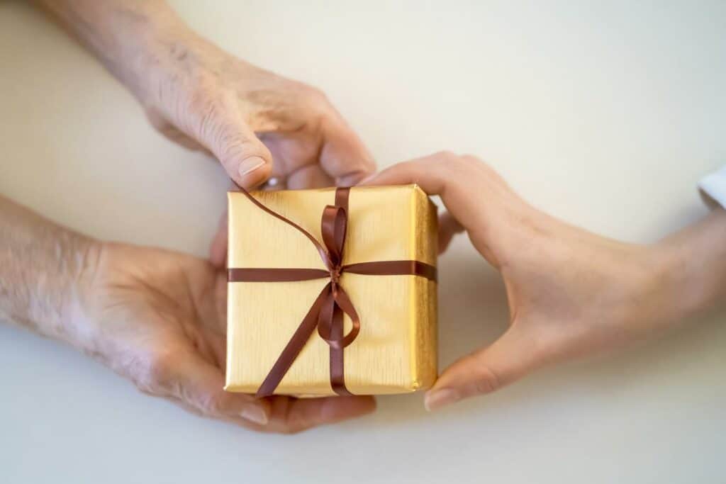 Hands of caregiver giving a new gift wrapped present into hands of a senior