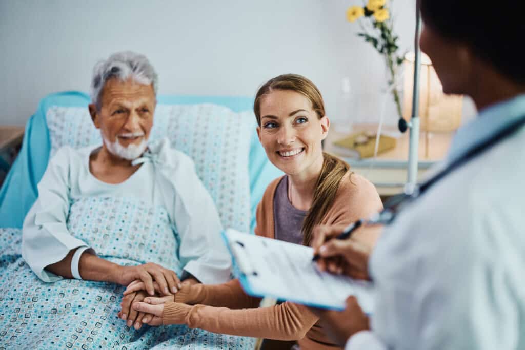 Woman in a hospital care room with her senior father in the hospital bed talking with a doctor