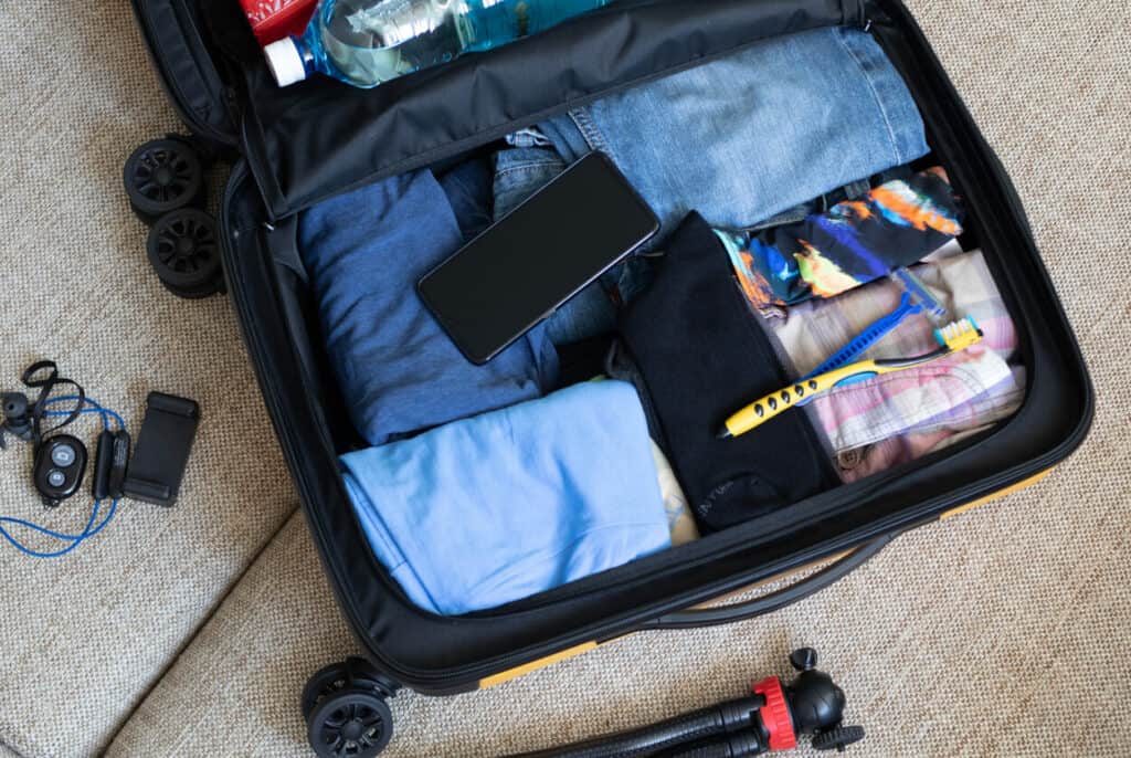 An open suitcase packed with clothes, a telephone, and a toothbrush