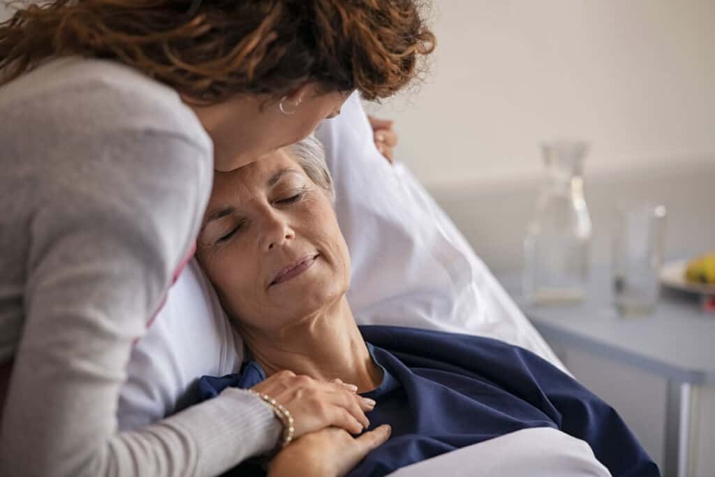 A woman giving a small kiss to her mother in a hospital bed