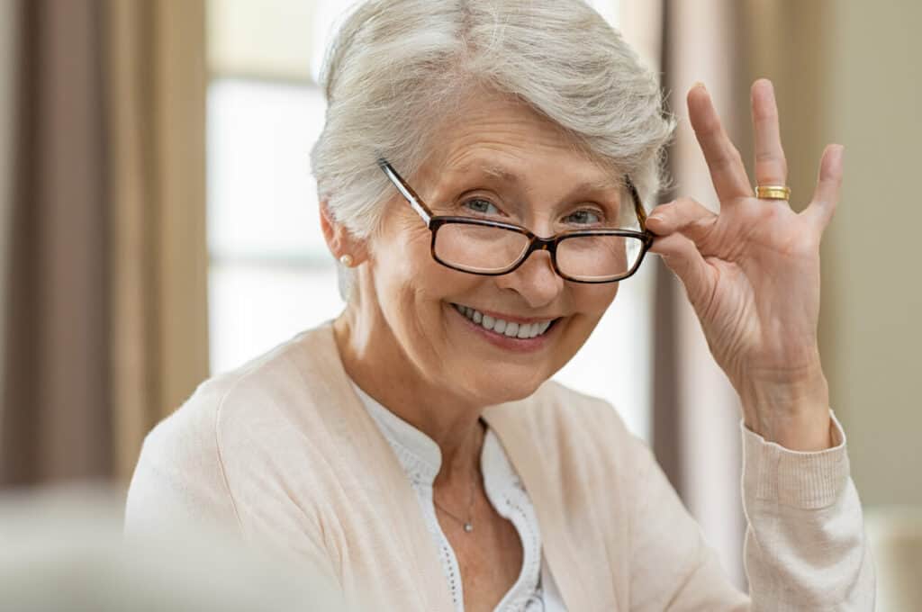 A smiling woman holding glasses to her eyes to read better.