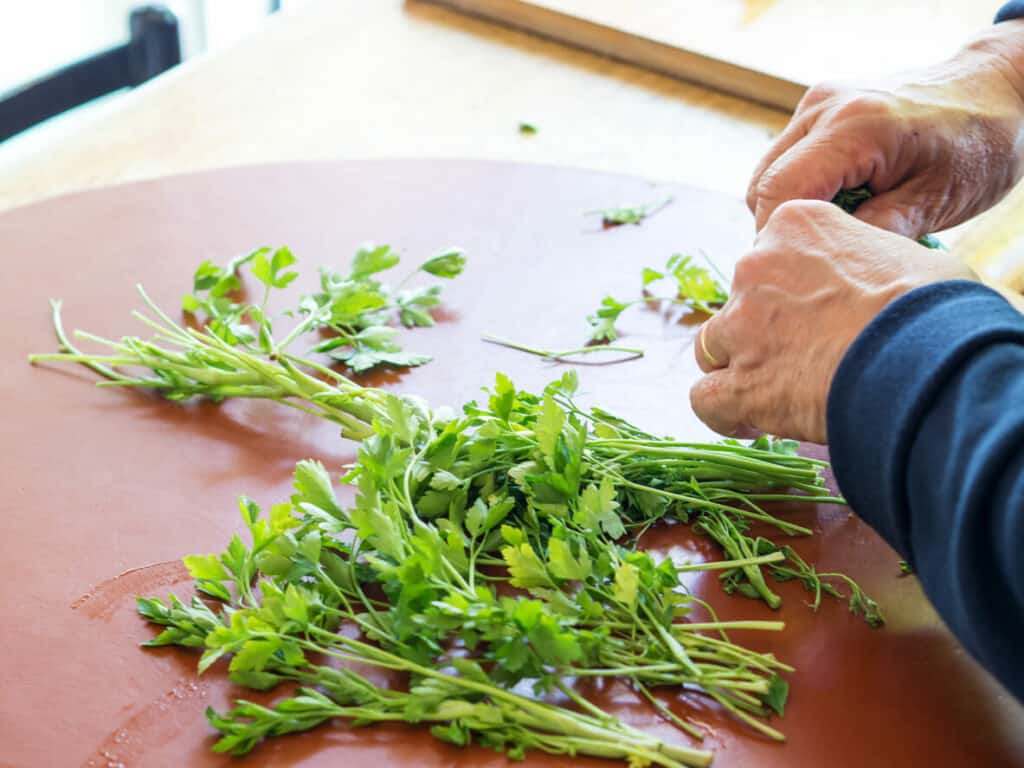 An elderly woman cutting herbs on a cutting board.