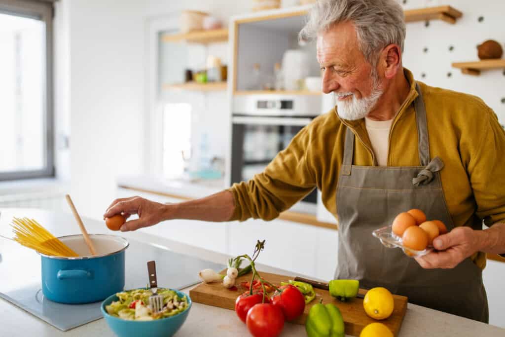 An older gentleman is cooking green vegetables and other healthy food.