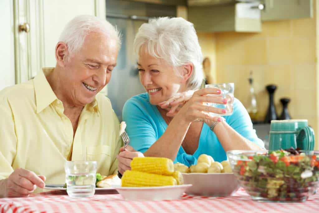 A senior couple eating a healthy meal together, smiling and looking at their food.