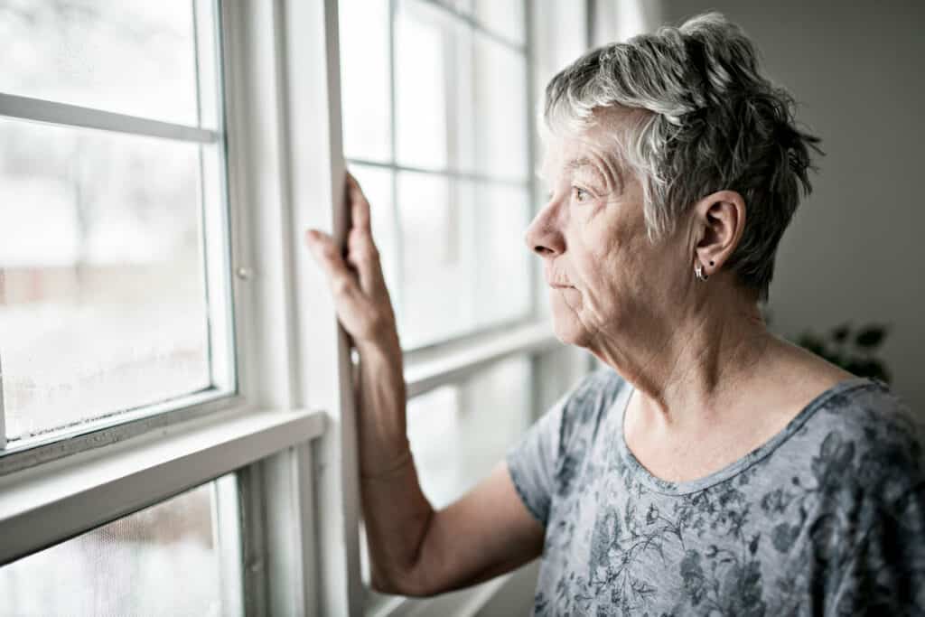 Woman with depression conditions looking through her home window