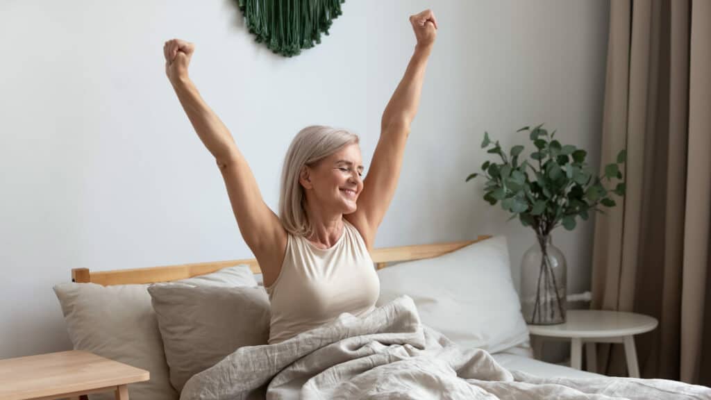 how much sleep does a 65 year old need? | elderly woman smiling as she wakes up well rested