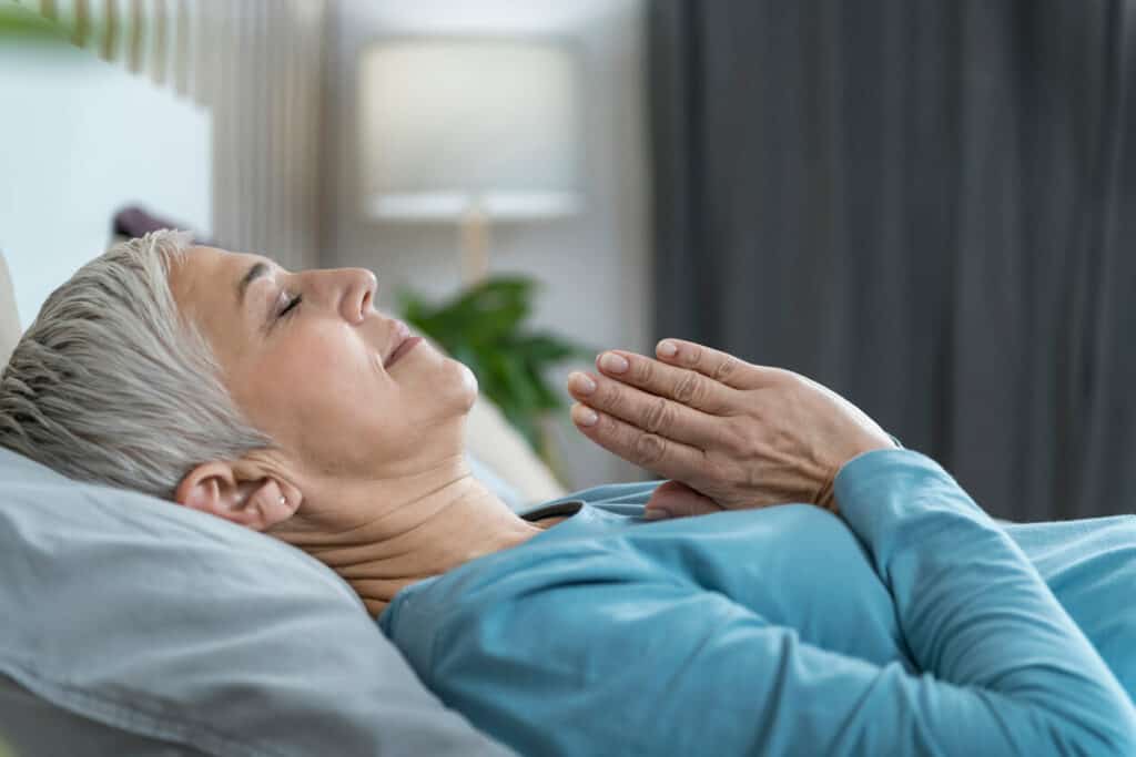 how much deep sleep do seniors need? | healthy elderly woman smiling and meditating in bed before sleeping