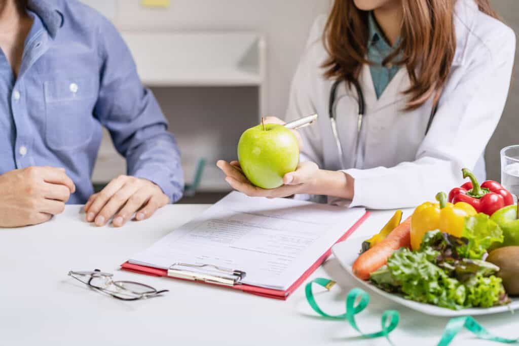 Questions to ask a nutritionist about diet. A photo of a female nutritionist holding a green apple during a patient consultation.