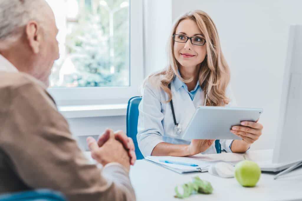 A senior man with nutrition questions to ask a smiling female nutritionist holding a tablet.