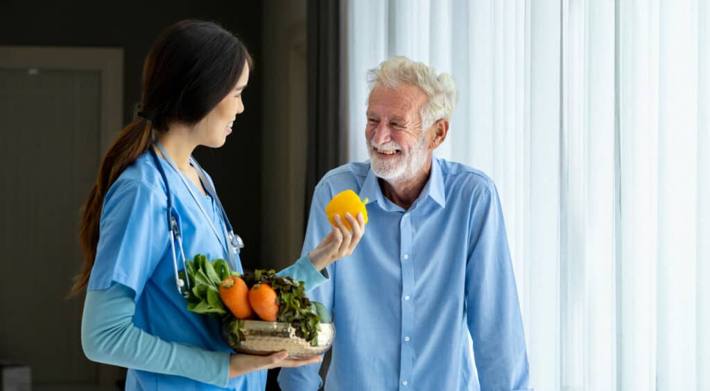 A senior man with nutrition questions to ask a female nutritionist holding a bowl of various vegetables.