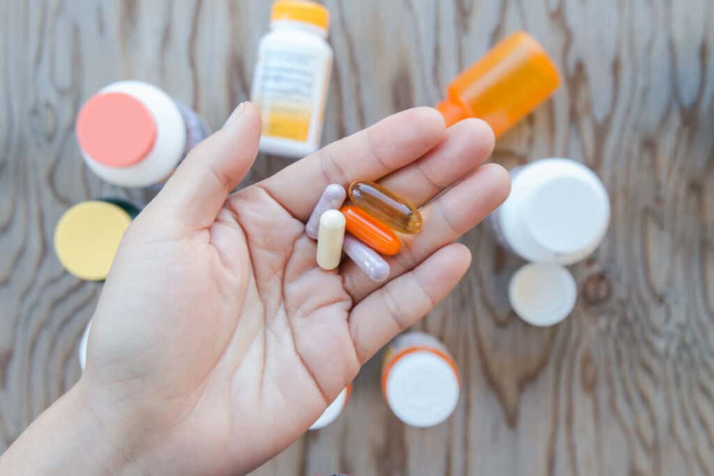 Questions to ask a nutritionist include what supplements to take. A photo of an open palm holding five different pills.