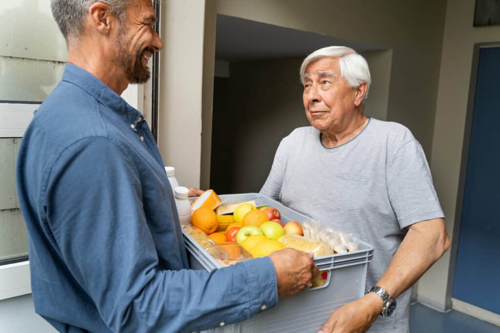 social services for elderly care - social worker helping an elderly man with groceries