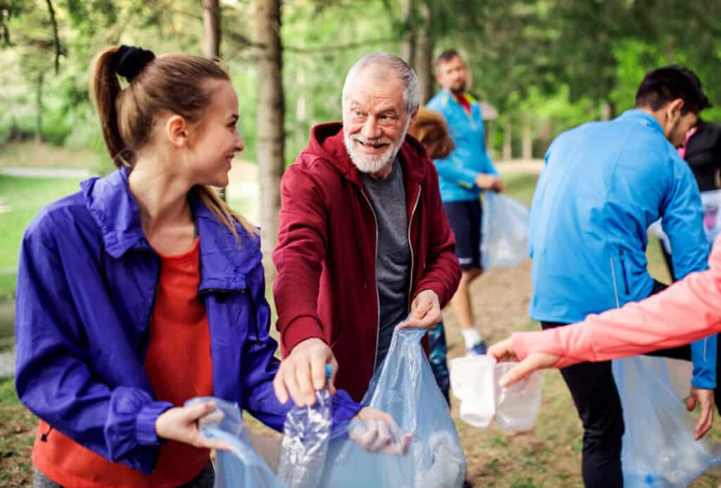 A senior man together with a group of young volunteers picking up litter.