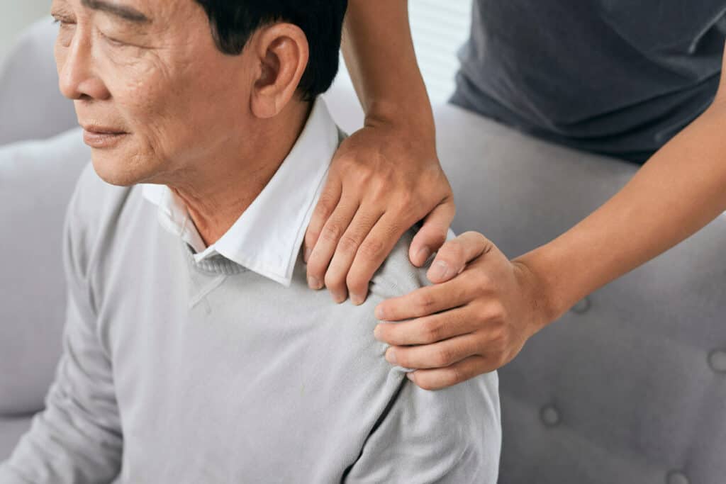 Therapist’s hands massaging the elderly man’s shoulder