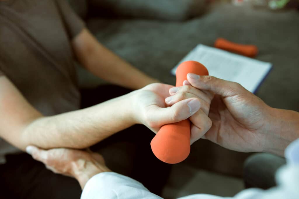 physical therapist helping patient hold a dumbbell in her hand