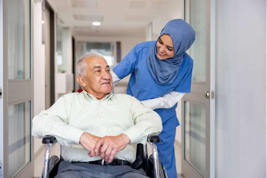 Female Muslim caregiver tending to a senior in a wheelchair in an elderly care home