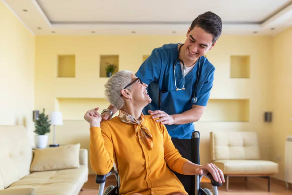 Male nursing assistant conducting a female senior in a wheelchair and taking care of her | elder care services jobs