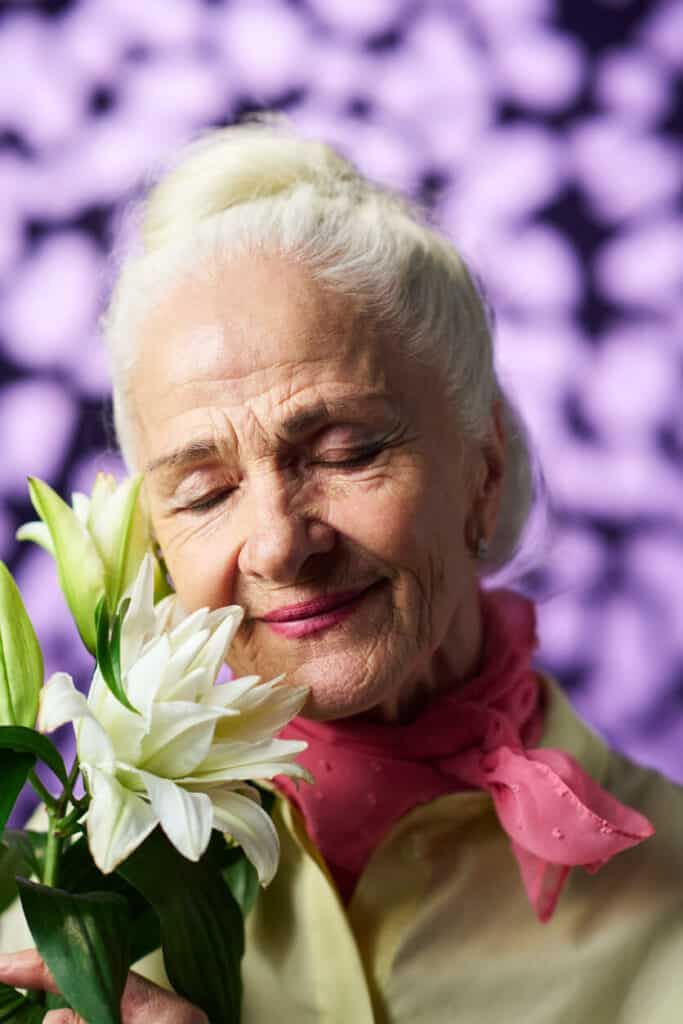 A smiling senior without nonenal odor smelling fresh flowers.