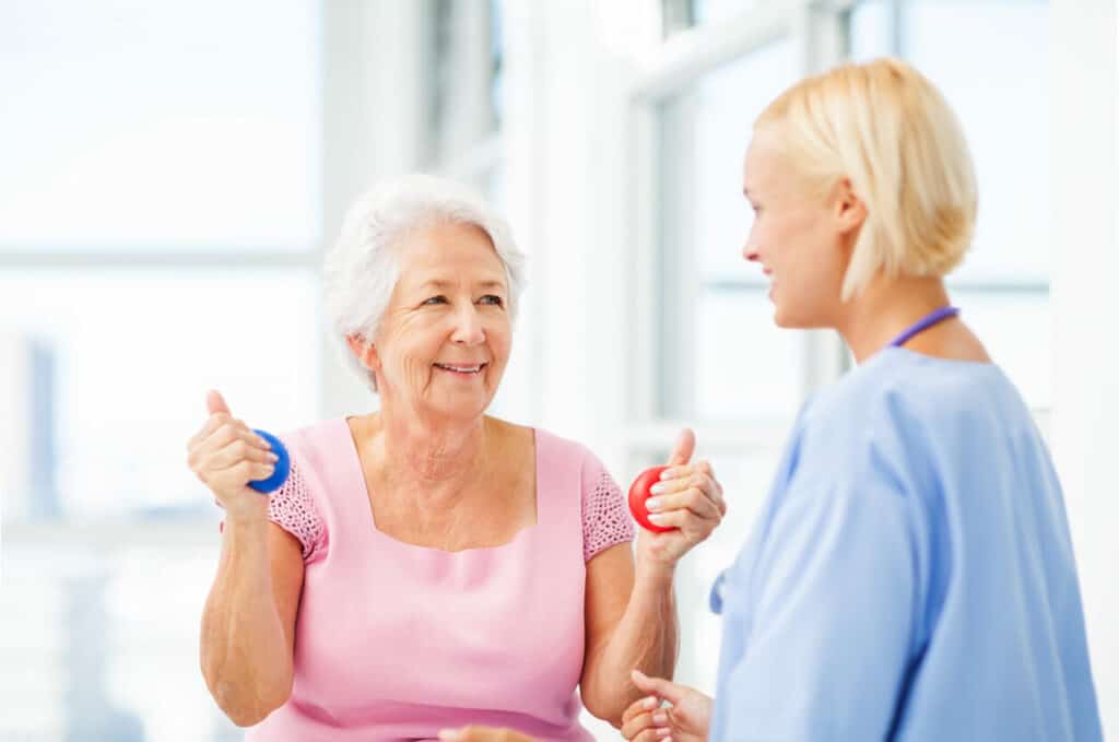 A female geriatric occupational therapist teaching a senior woman some hand exercises.