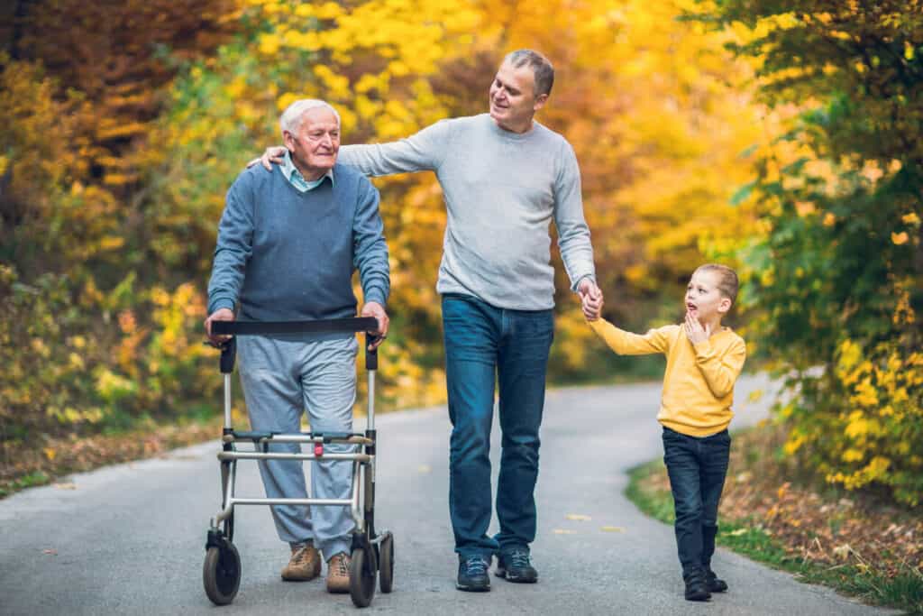 A son and a grandson walk with an older grandfather with Alzheimer’s down the street. Everyone is smiling and happy to be together.| alzheimer ronald reagan