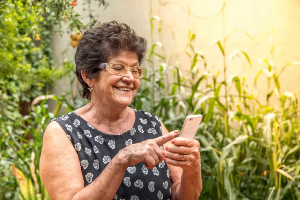 Elderly woman using a cell phone and smiling | in-home computer help for seniors