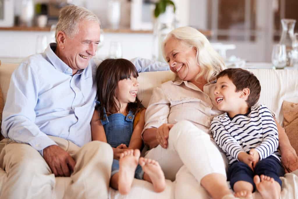 What year did Grandparents Day start - A smiling senior couple sitting on a sofa with their grandchildren.