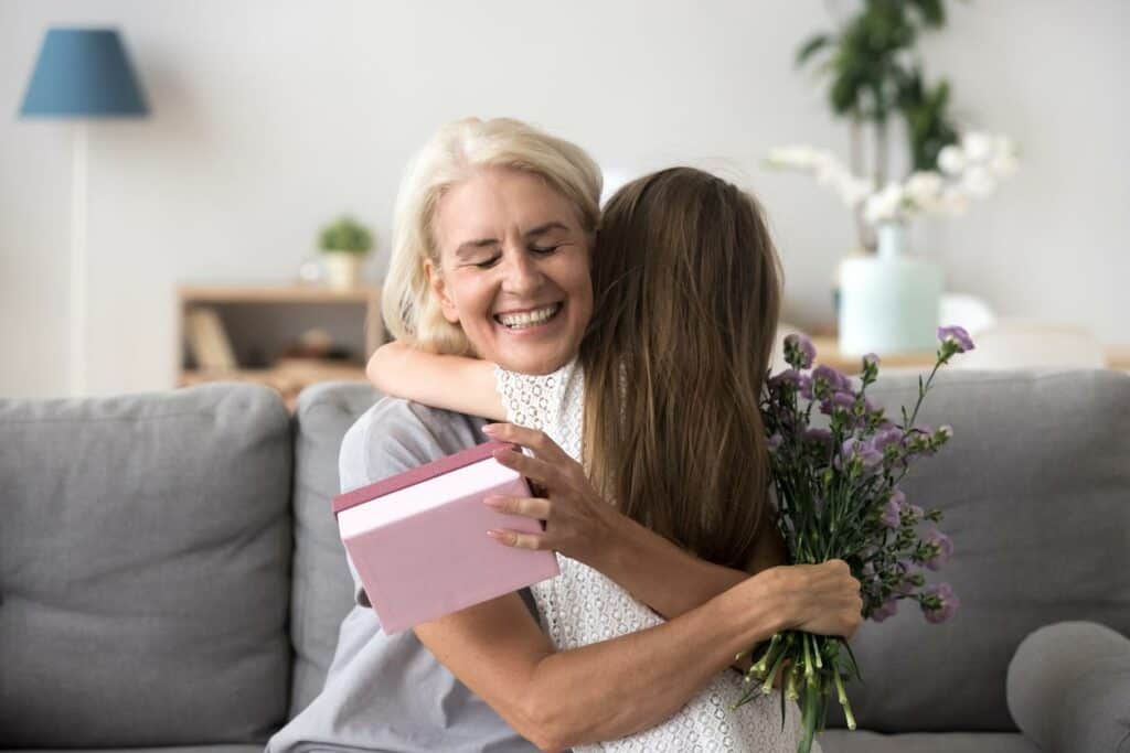 When did Grandparents Day begin - a grandmother hugging her granddaughter, holding in her hand some flowers and a present.