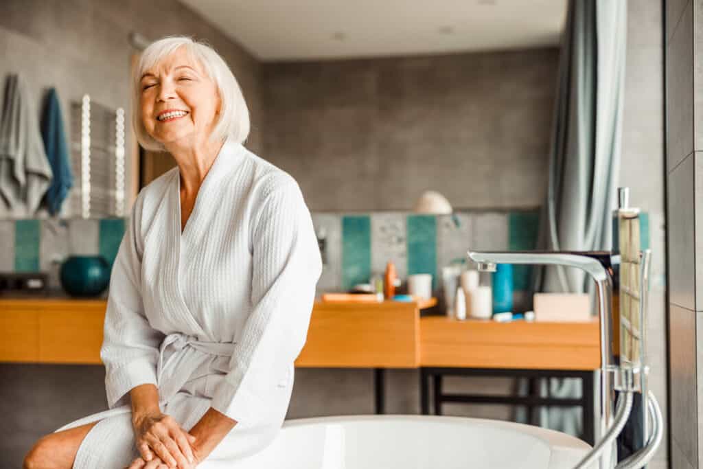 Elderly shower assistance - a senior smiling while sitting at the edge of the bathtub