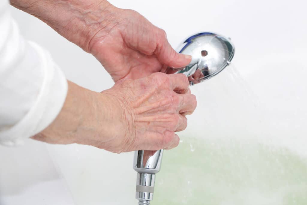 Elderly shower assistance - a senior woman’s hand holding a handheld shower head