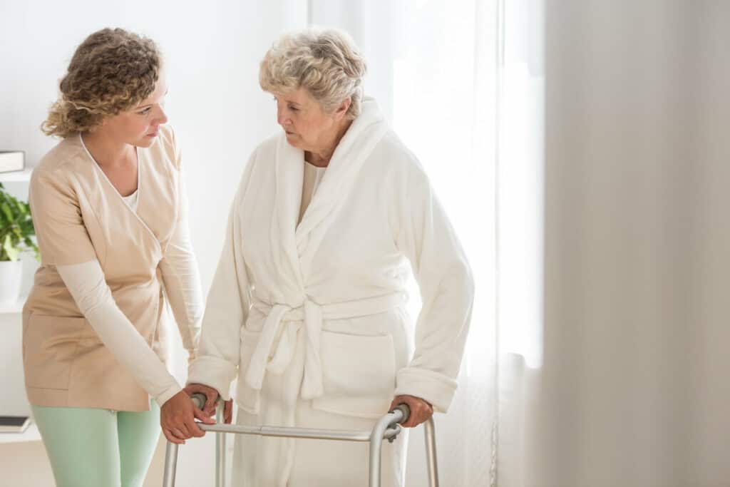 Bathing assistance elderly - a caregiver and a senior woman using a walker in a bathrobe walking to the bathroom