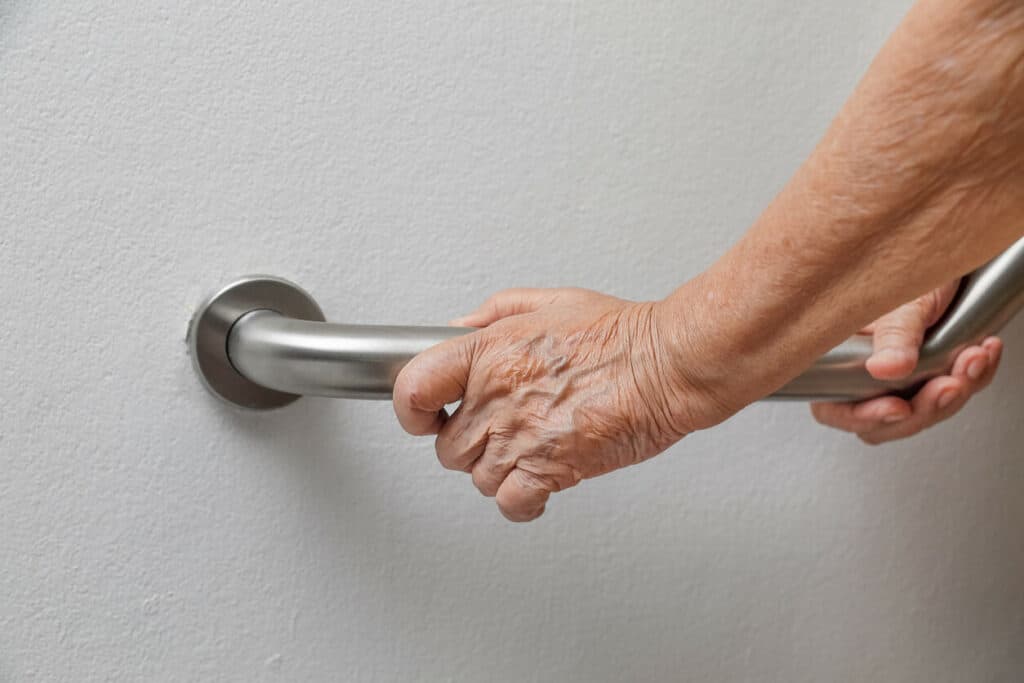 An older woman holding a grab bar for stability and support when using the bathroom - caring for mom