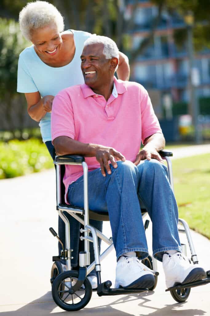 A spouse caregiver pushing the wheelchair of her husband through a park
