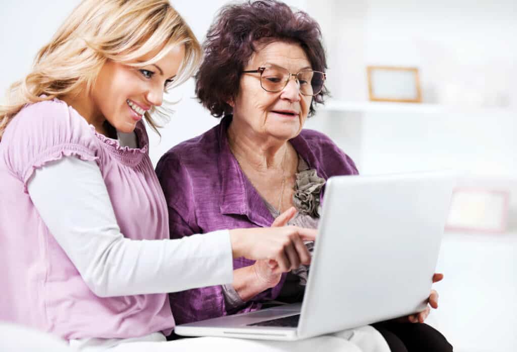 A daughter teaching her senior mom how to search for caregiving courses online to be a spousal caregiver
