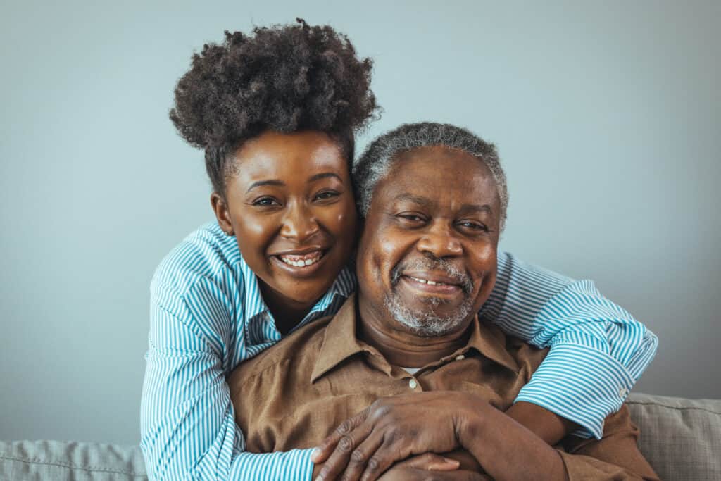 Black male senior being hugged by her daughter while receiving in-home Parkinsons care
