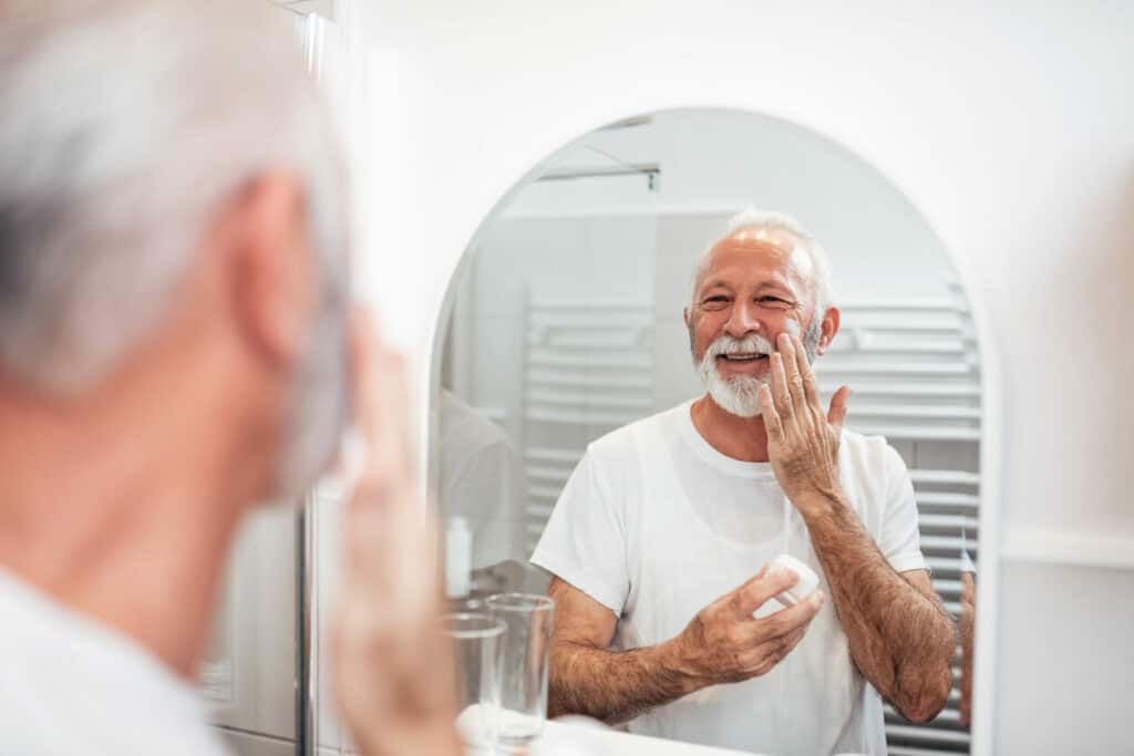 Senior male with PD grooming his beard in front of the mirror. Giving our loved one adequate tools to care for themselves is a good Parkinson’s homecare idea.