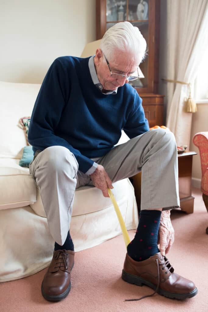 A senior man putting on his shoes using a long handled shoe horn - Parkinsons home care.