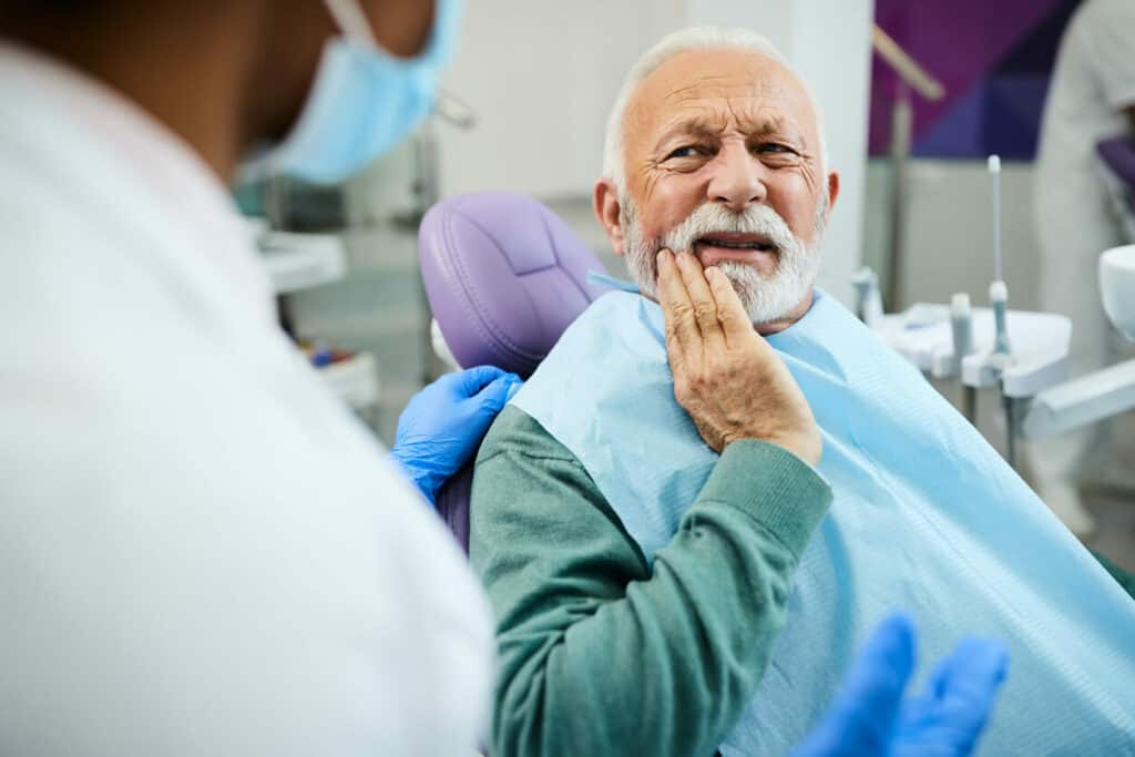 aging taste buds - older adult at the dentist chair holding his lower jaw in pain