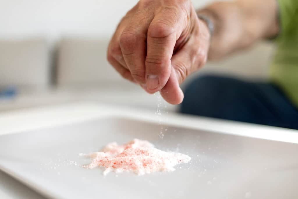 higher salt intake is a reason for the reduction in taste sensitivity among older adults - a male’s hand holding a pinch of salt over a small pile of salt