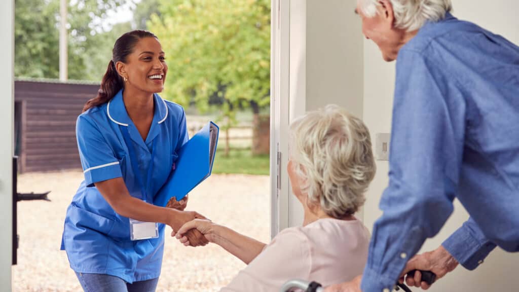 Female senior occupational therapist is entering an elderly’s home and shaking hands